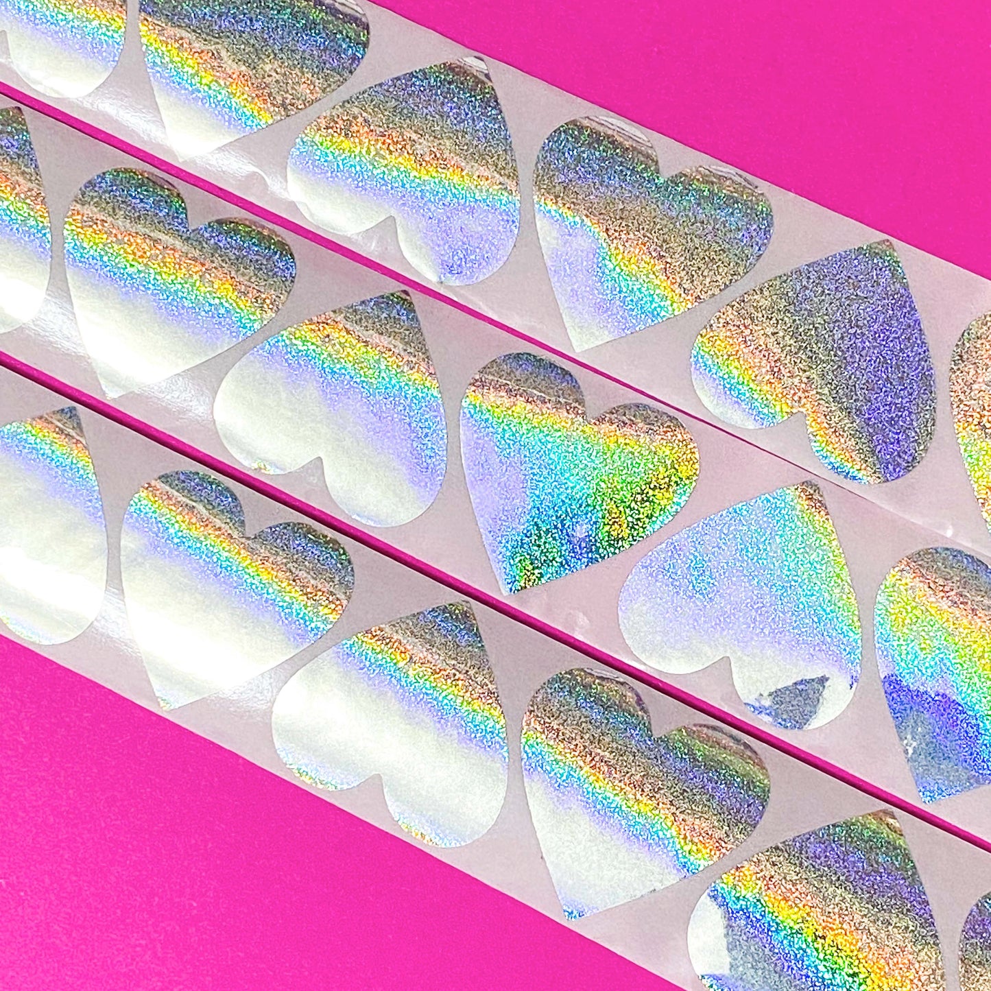Holographic large 38mm silver heart-shaped stickers with rainbow glitter on a pink background