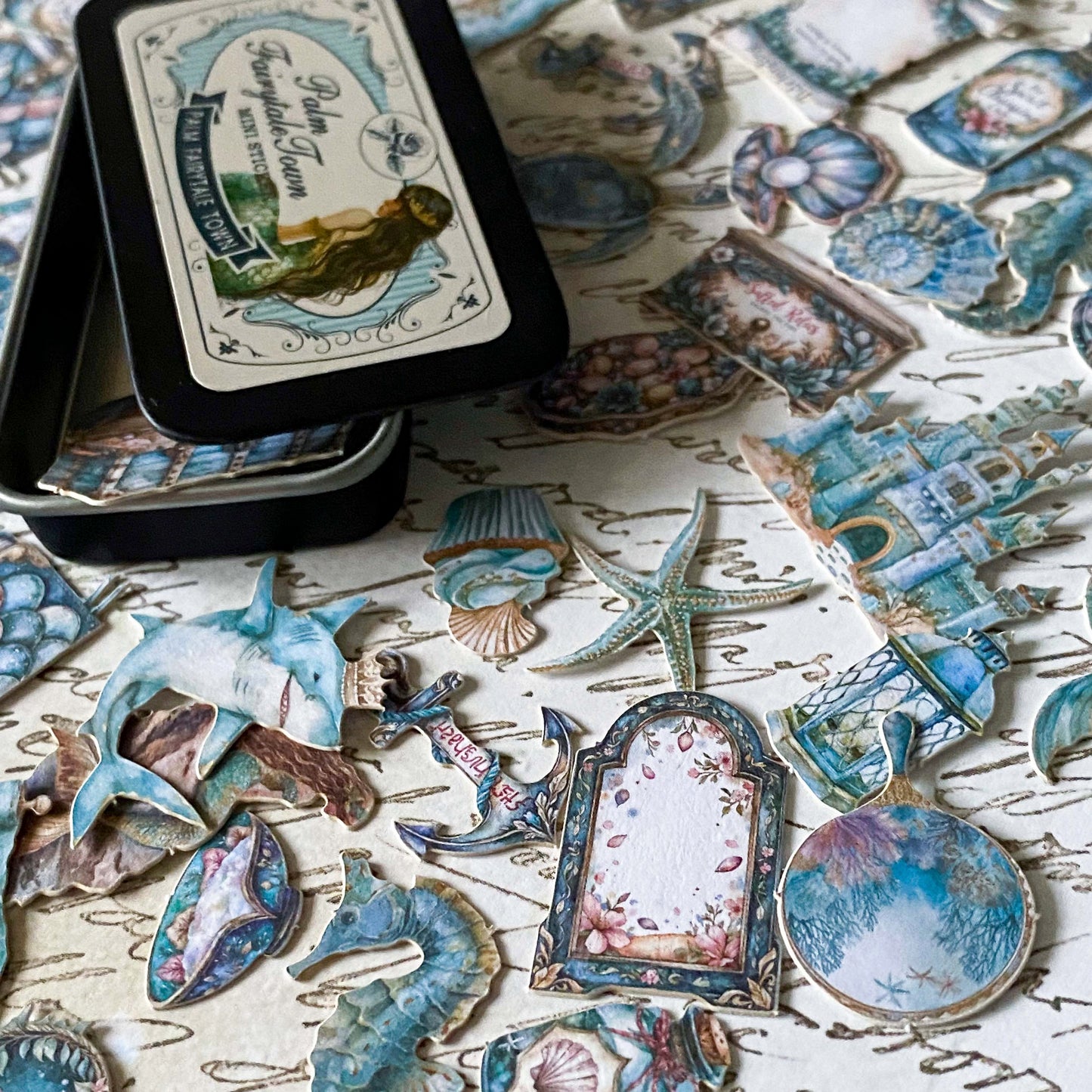 mini metal tin of 60 small card stickers in an ocean mermaid theme with caskets, treasure, shells, starfish and books.