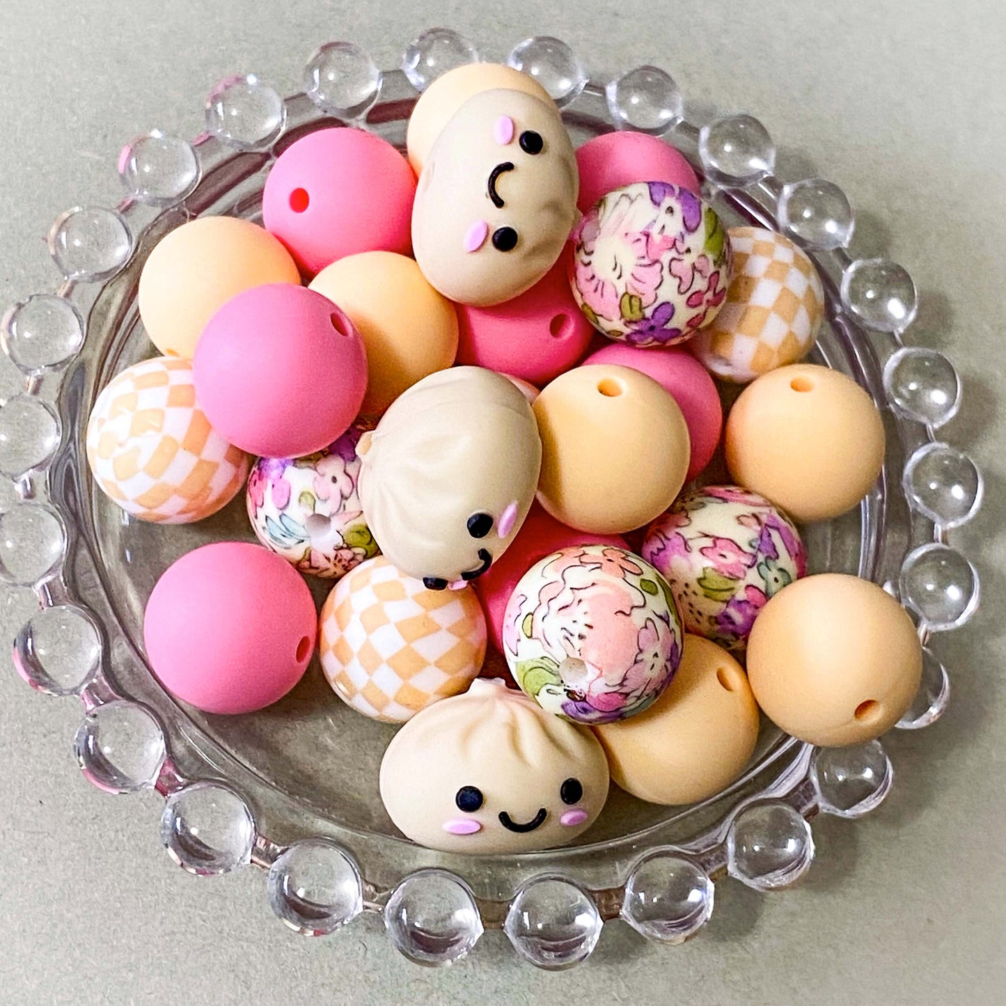 a coordinated bundle of 8 pastel silicone beads featuring one smiling jumbo dumpling bead, floral patterned beads and checkerboard beads, plain pink and cream beads. uk craft supplies.
