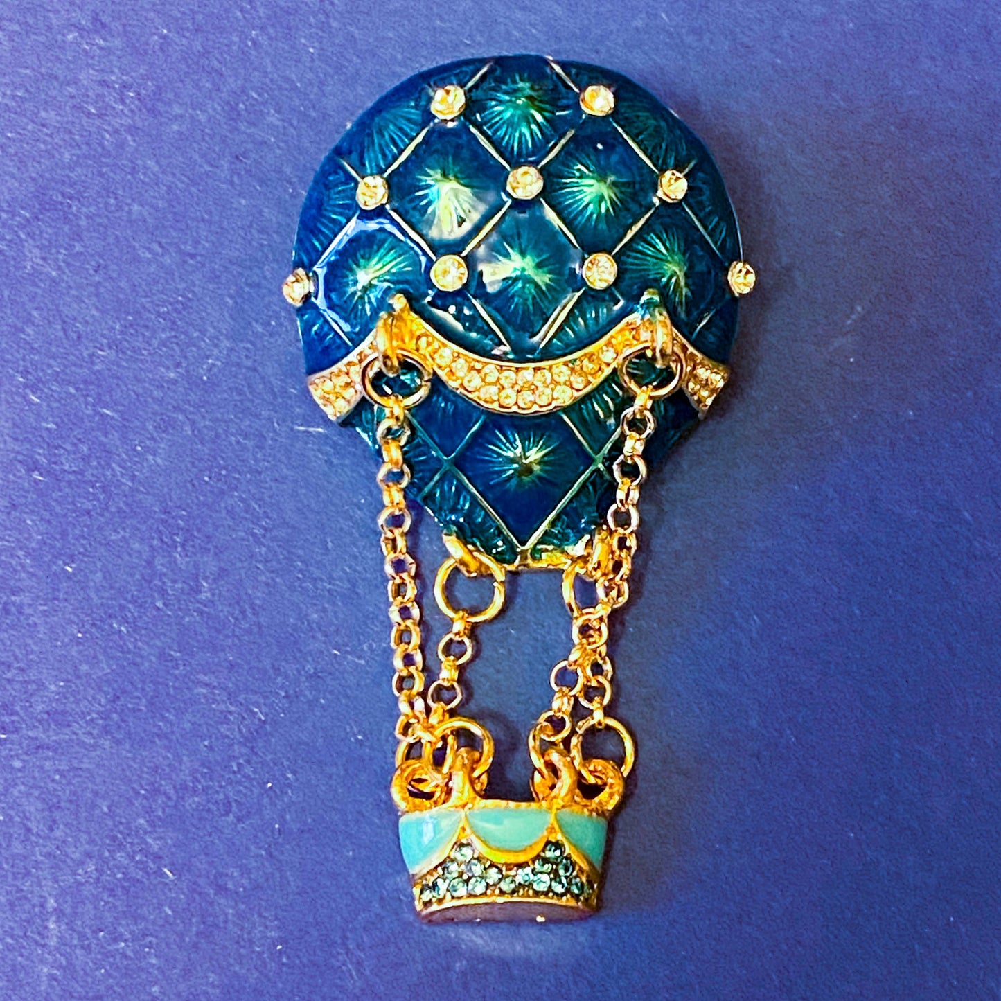 Decorative brooch shaped like a hot air balloon with blue and gold design on a blue background