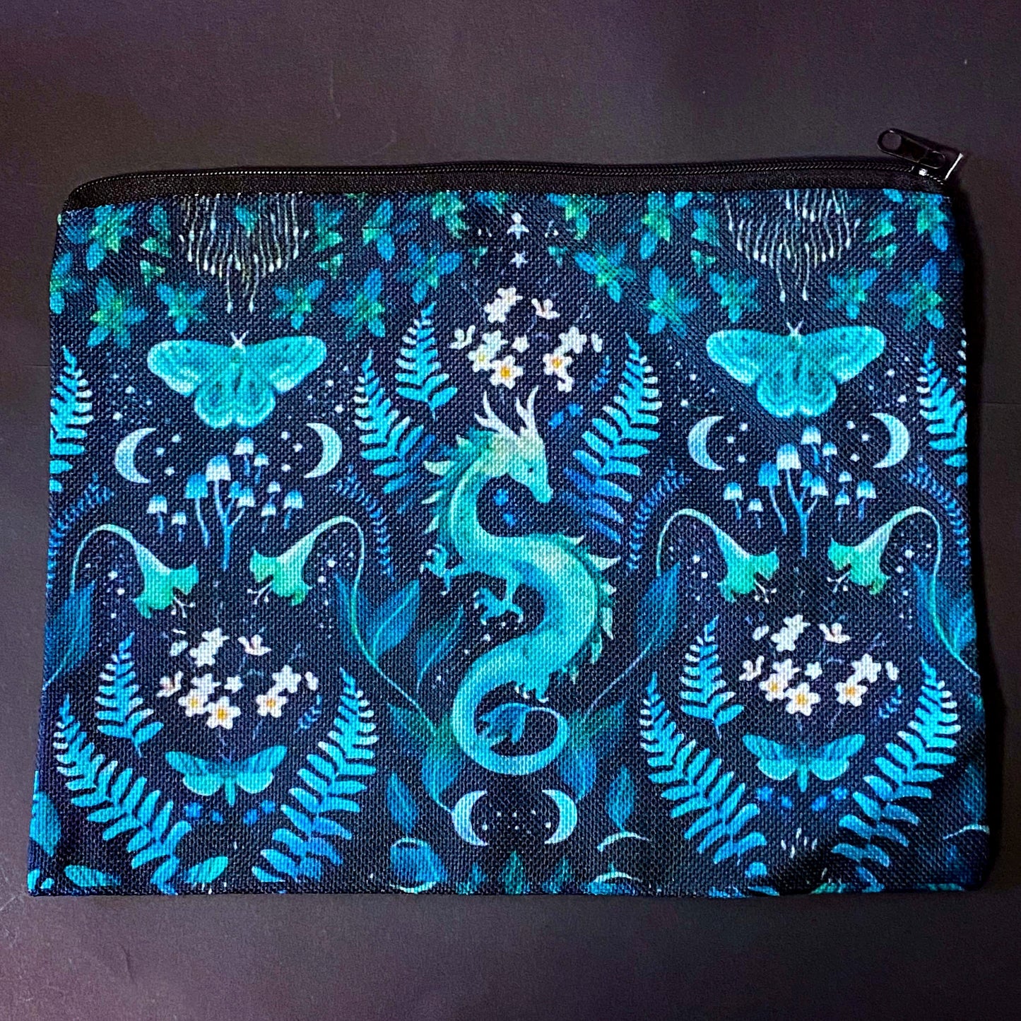 twilight fern dragon fabric zip pouch featuring a turquoise dragon surrounded by ferns, butterflies, flowers, mushrooms and crescent moons on a black background. turquoise, teal and mint green cosmetic bag.
