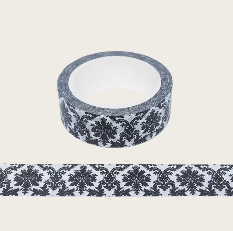 A 10m roll of decorative washi tape with a black and white damask pattern, shown with a strip of the tape unrolled below on a light beige background.