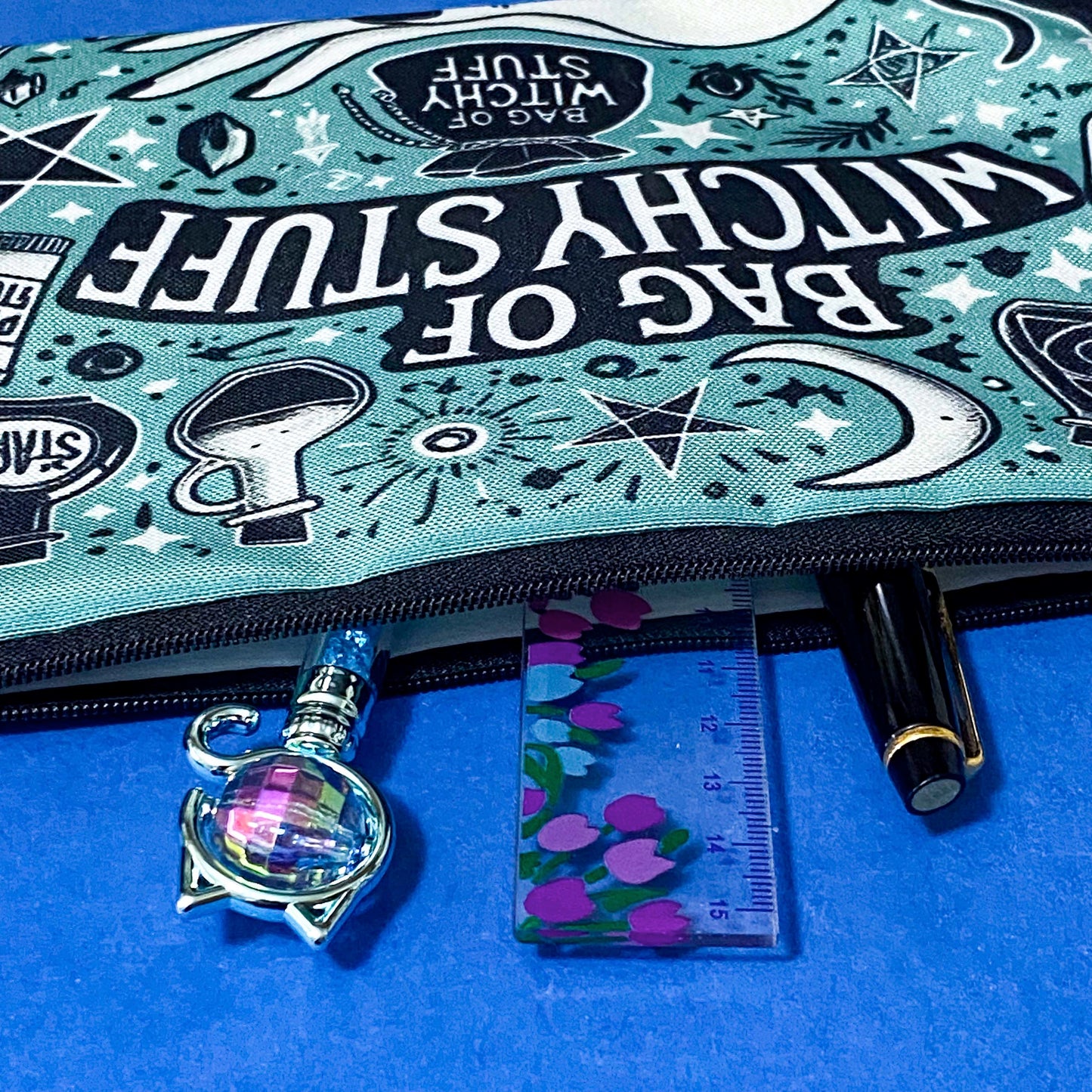 turquoise and black canvas zip pouch featuring the words "Bag of witchy stuff" surrounded by potion bottles, moons, stars, crystals and magical symbols. Uk cute and kawaii gifts shop. Bag for journaling, crystal storage or witchcraft supplies.
