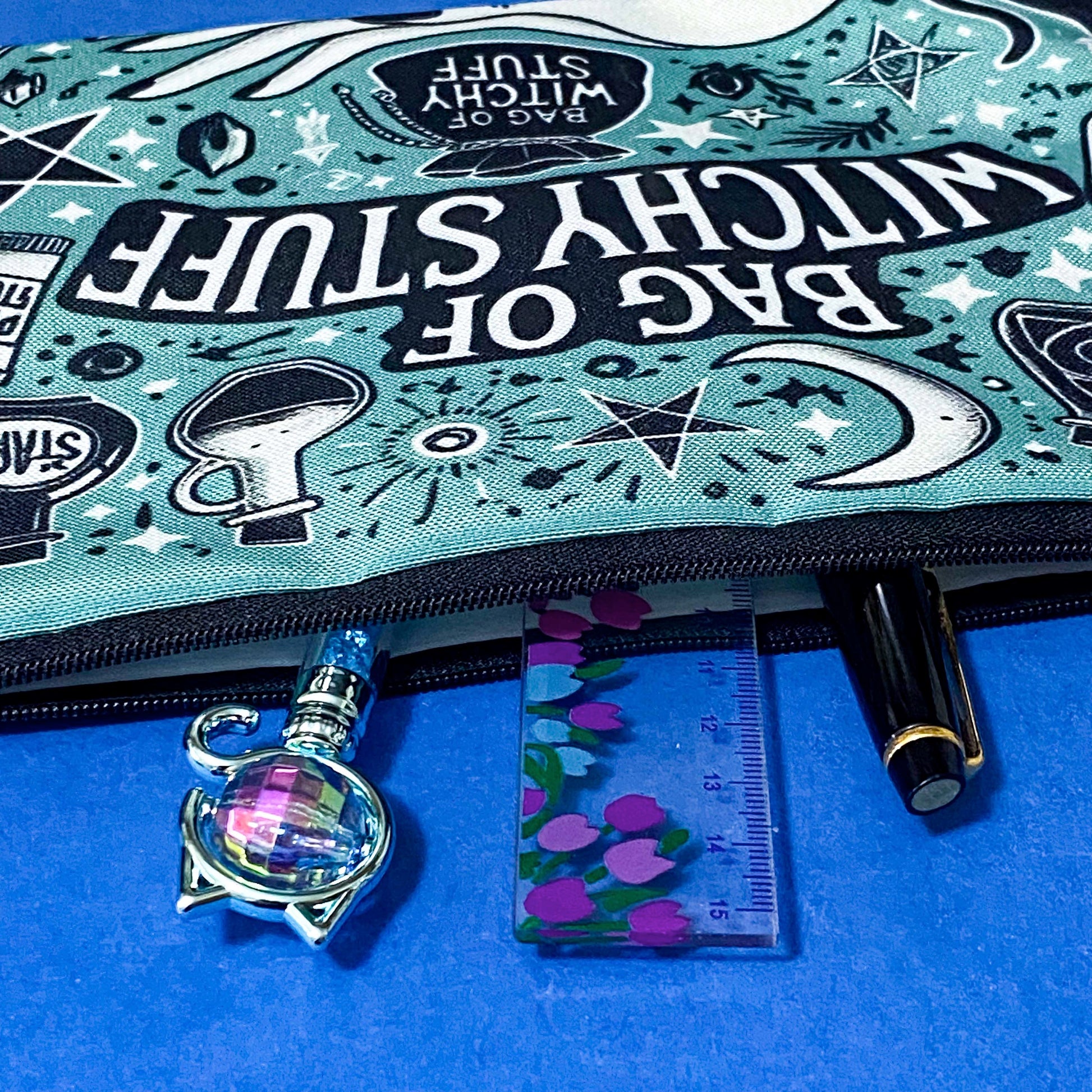 turquoise and black canvas zip pouch featuring the words "Bag of witchy stuff" surrounded by potion bottles, moons, stars, crystals and magical symbols. Uk cute and kawaii gifts shop. Bag for journaling, crystal storage or witchcraft supplies.