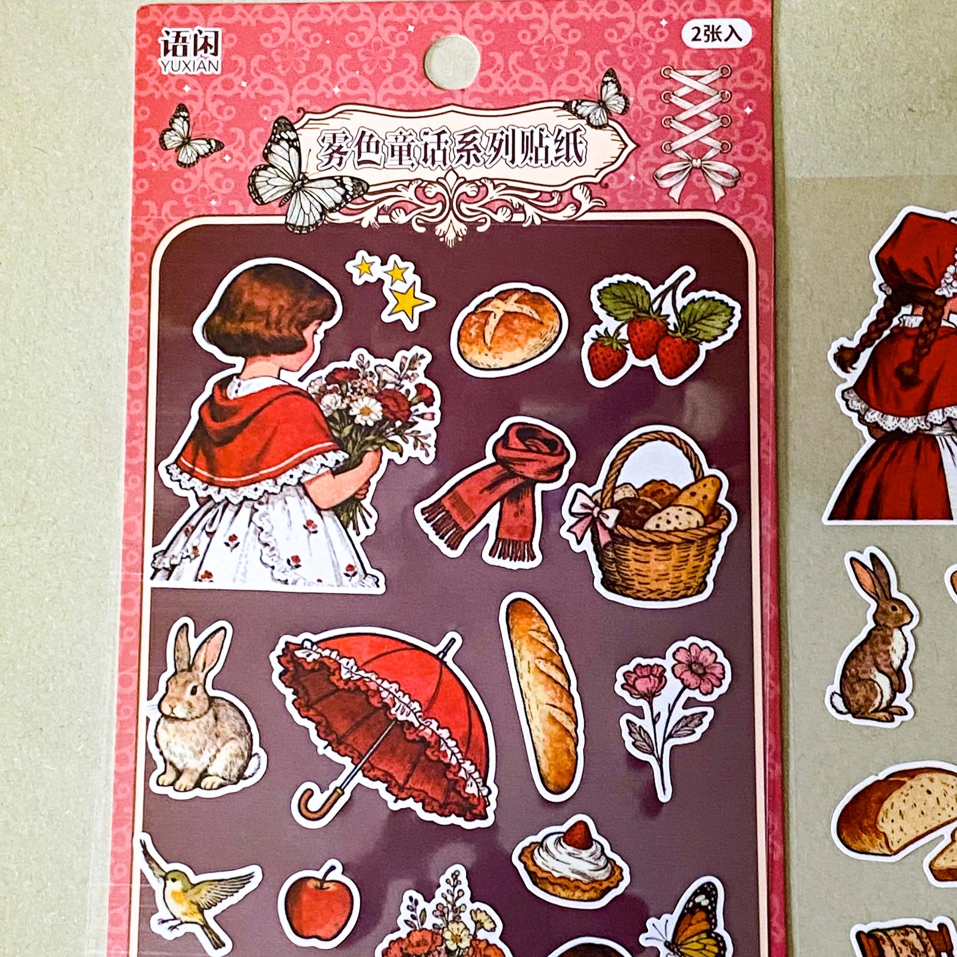 red riding hood's cottage matte sticker pack with two decorative clear sheets of stickers featuring little red riding hood, woodland animals, cottages, flowers, baskets, books, strawberries, squirrels, rabbits and cosy cottagecore illustrations.