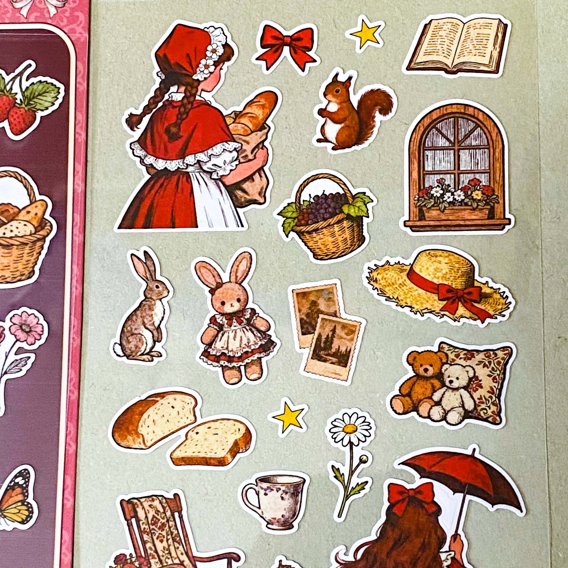 red riding hood's cottage matte sticker pack with two decorative clear sheets of stickers featuring little red riding hood, woodland animals, cottages, flowers, baskets, books, strawberries, squirrels, rabbits and cosy cottagecore illustrations.