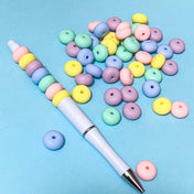 silicone pastel spacer beads with a beaded pen on a blue background