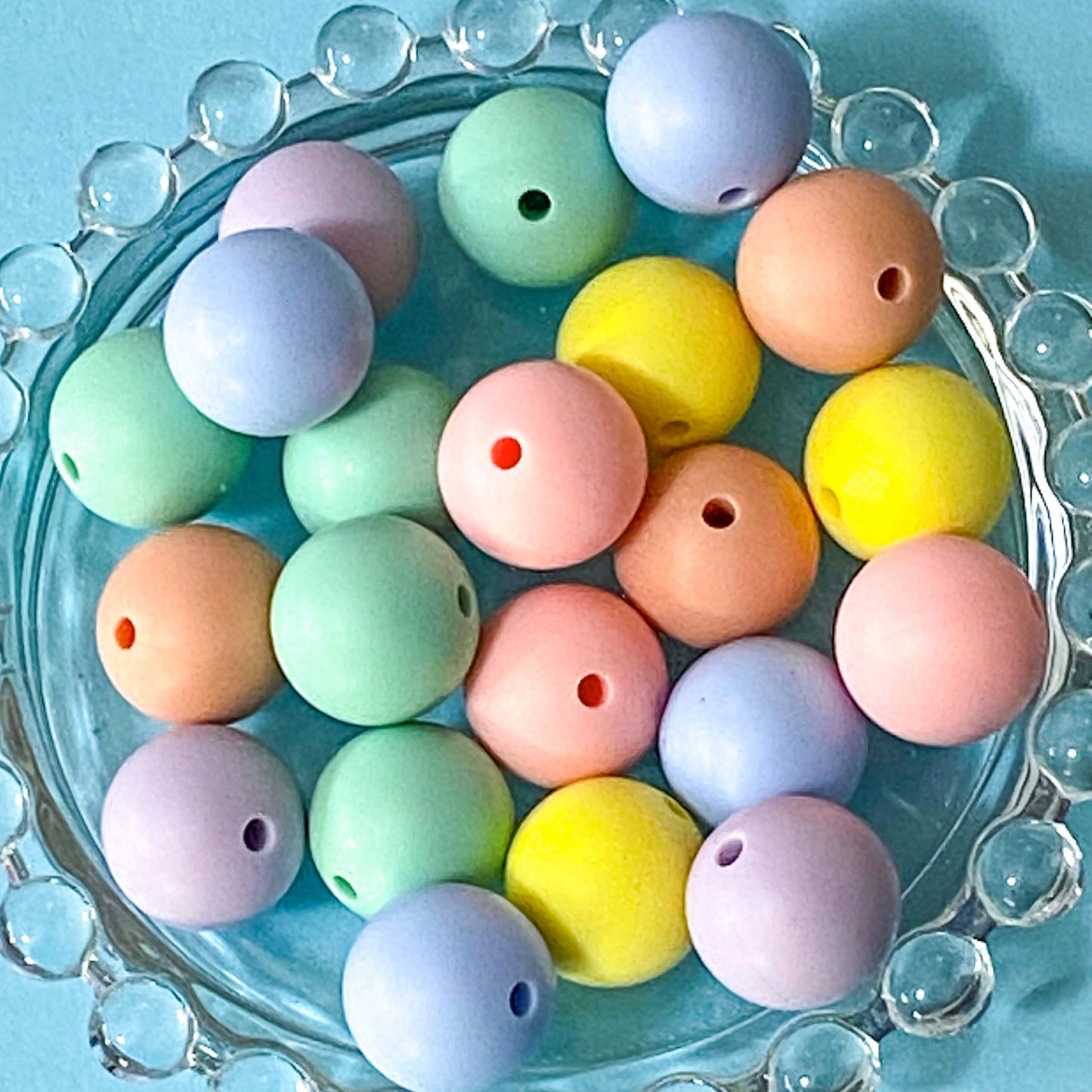 Pastel-colored 16mm round plain silicone beads on a decorative glass plate with a blue background