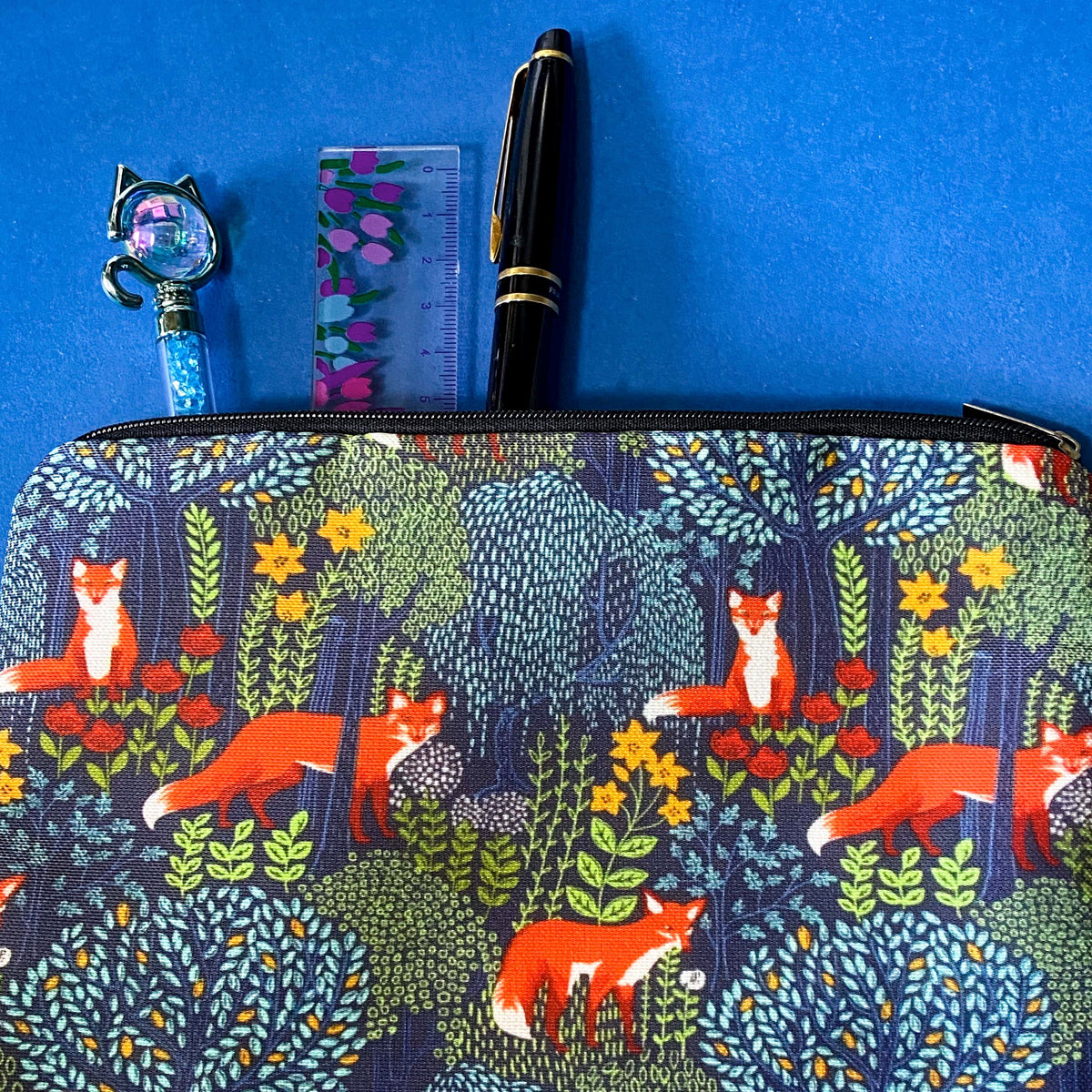 midnight fox hollow canvas fabric pouch featuring orange foxes among wildflowers and trees on a navy background. Zip make up cosmetic bag or journaling pouch. UK cute gift shop.