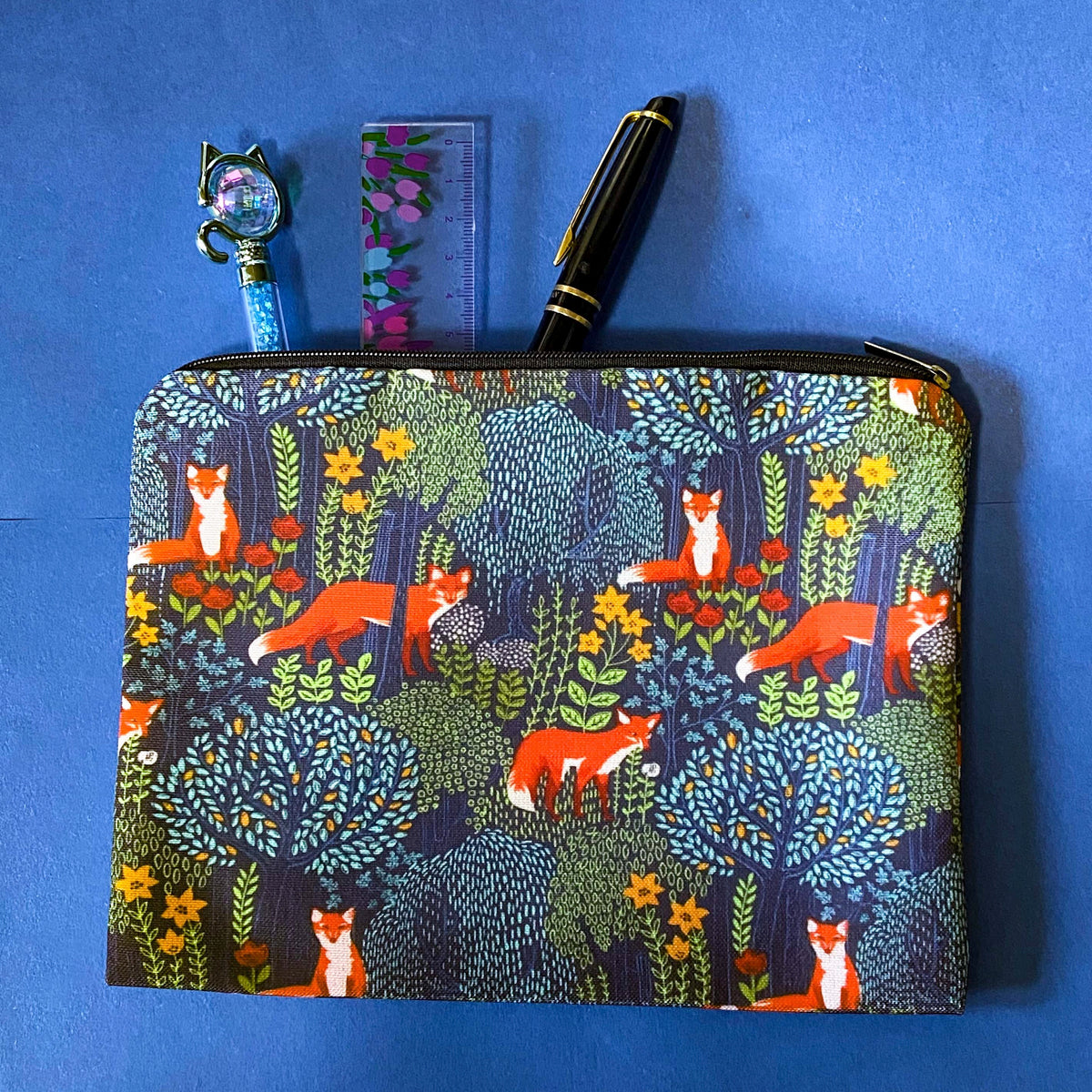 midnight fox hollow canvas fabric pouch featuring orange foxes among wildflowers and trees on a navy background. Zip make up cosmetic bag or journaling pouch. UK cute gift shop.