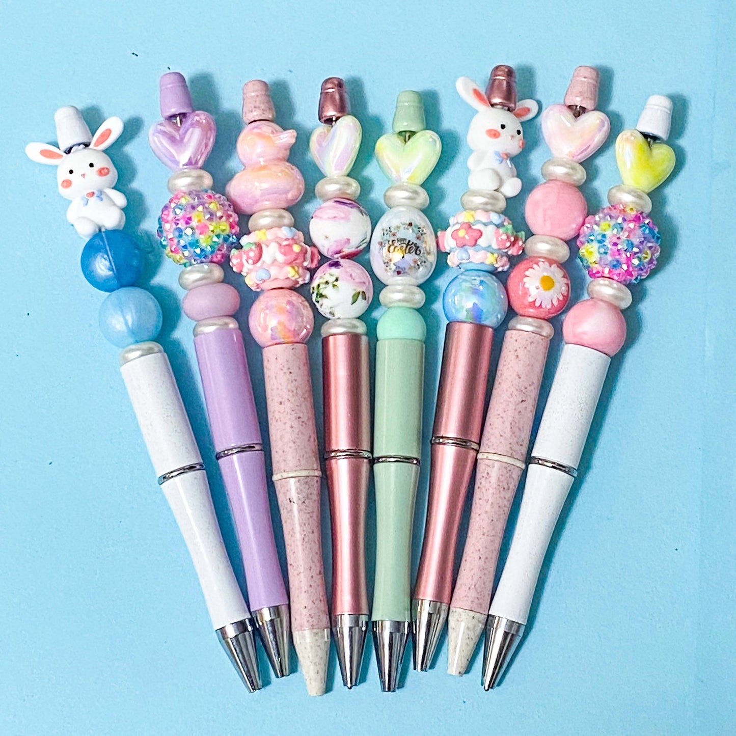 Decorative pen kits with colourful beads and spring bunny toppers on a blue background