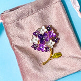 Purple and white floral metal and enamel hydrangea brooch on a pink velvet surface with a blue background