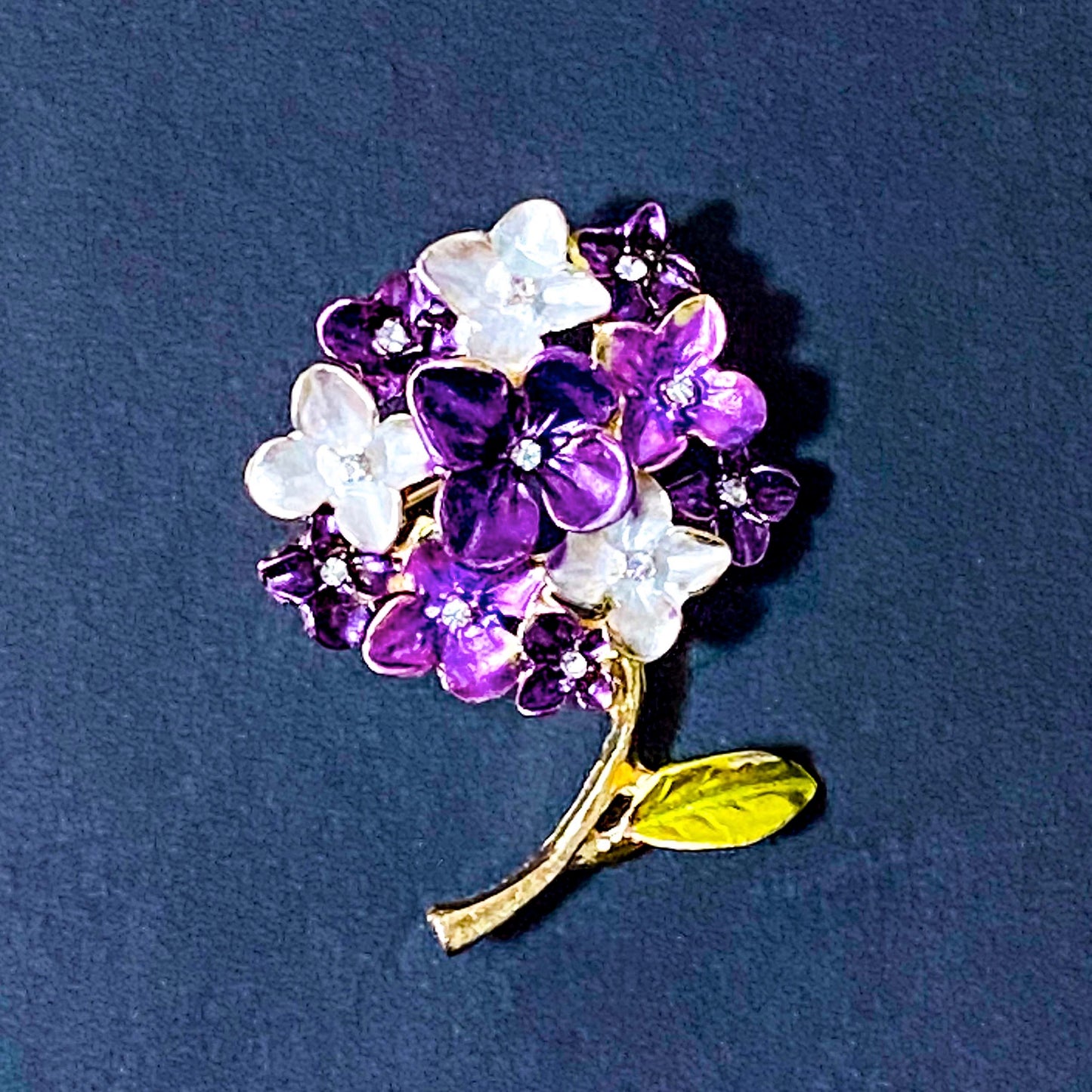 Floral hydrangea brooch with purple and white flowers on a dark blue background
