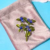 Brooch with blue berries and green leaves on a pink fabric background