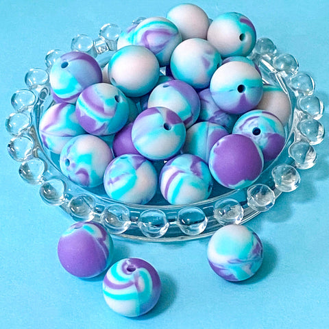 Marbled purple and blue large silicone beads on a clear glass plate against a blue background