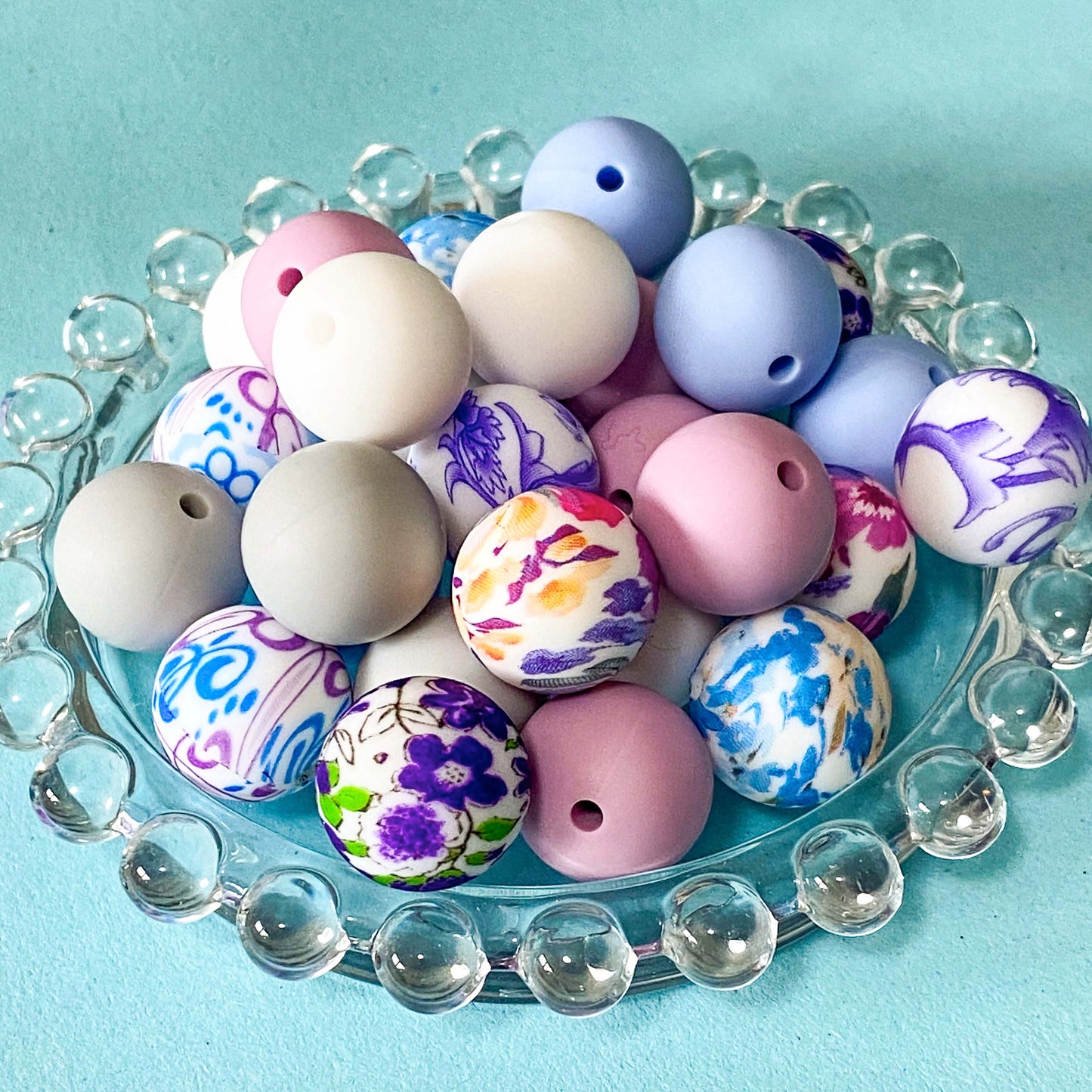 floral and plain round silicone 16mm beads in pretty pastel colours of pink, lilac, blue and white on a glass plate