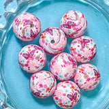 Decorative pink silicone beads with floral and butterfly patterns on a blue plate