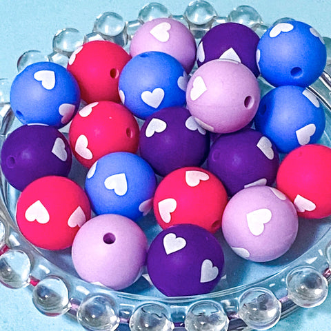 Colourful 16mm silicone beads with white heart patterns on a clear stand against a light blue background