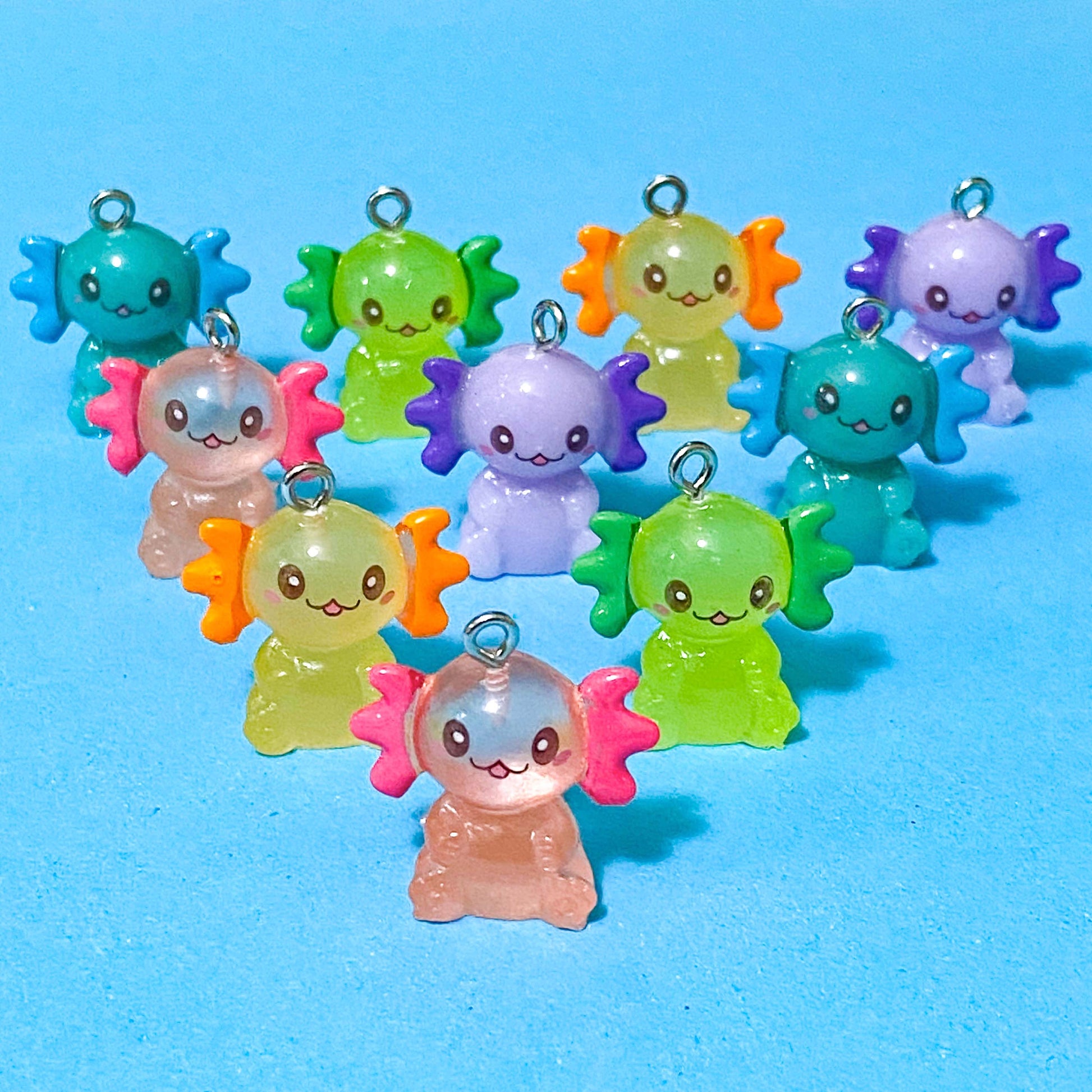 translucent resin and acrylic axolotl glow in the dark charms with silver metal hooks and measuring 25mm tall. uk cute craft supplies for jewellery making. pink, orange, lime green, lilac and turquoise axolotls.