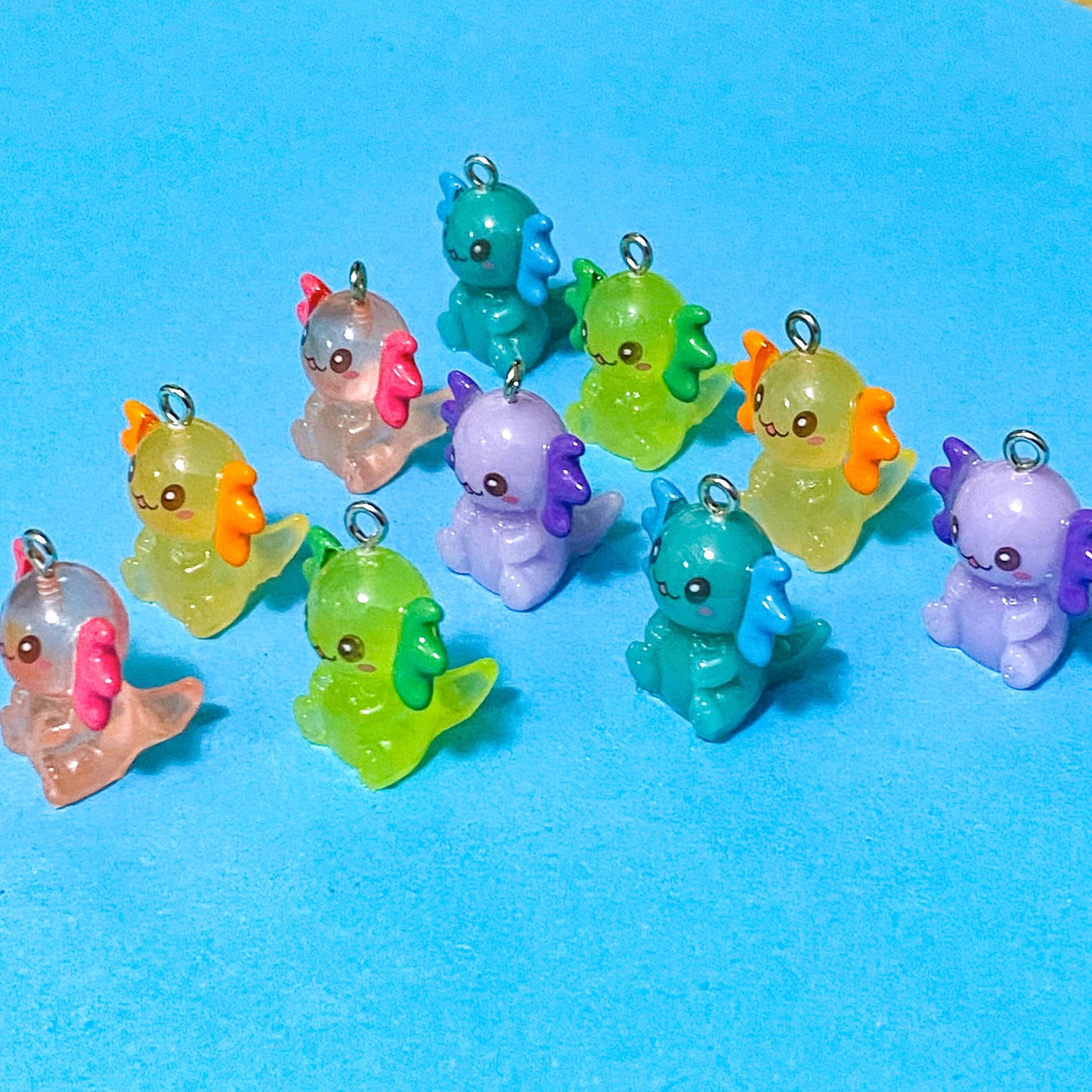 translucent resin and acrylic axolotl glow in the dark charms with silver metal hooks and measuring 25mm tall. uk cute craft supplies for jewellery making. pink, orange, lime green, lilac and turquoise axolotls.