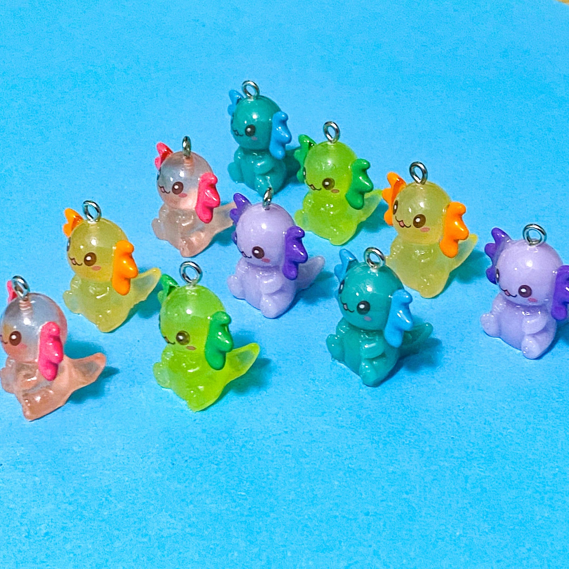 translucent resin and acrylic axolotl glow in the dark charms with silver metal hooks and measuring 25mm tall. uk cute craft supplies for jewellery making. pink, orange, lime green, lilac and turquoise axolotls.