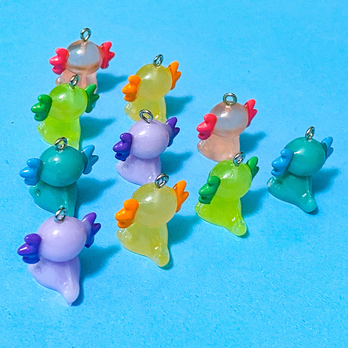 translucent resin and acrylic axolotl glow in the dark charms with silver metal hooks and measuring 25mm tall. uk cute craft supplies for jewellery making. pink, orange, lime green, lilac and turquoise axolotls.