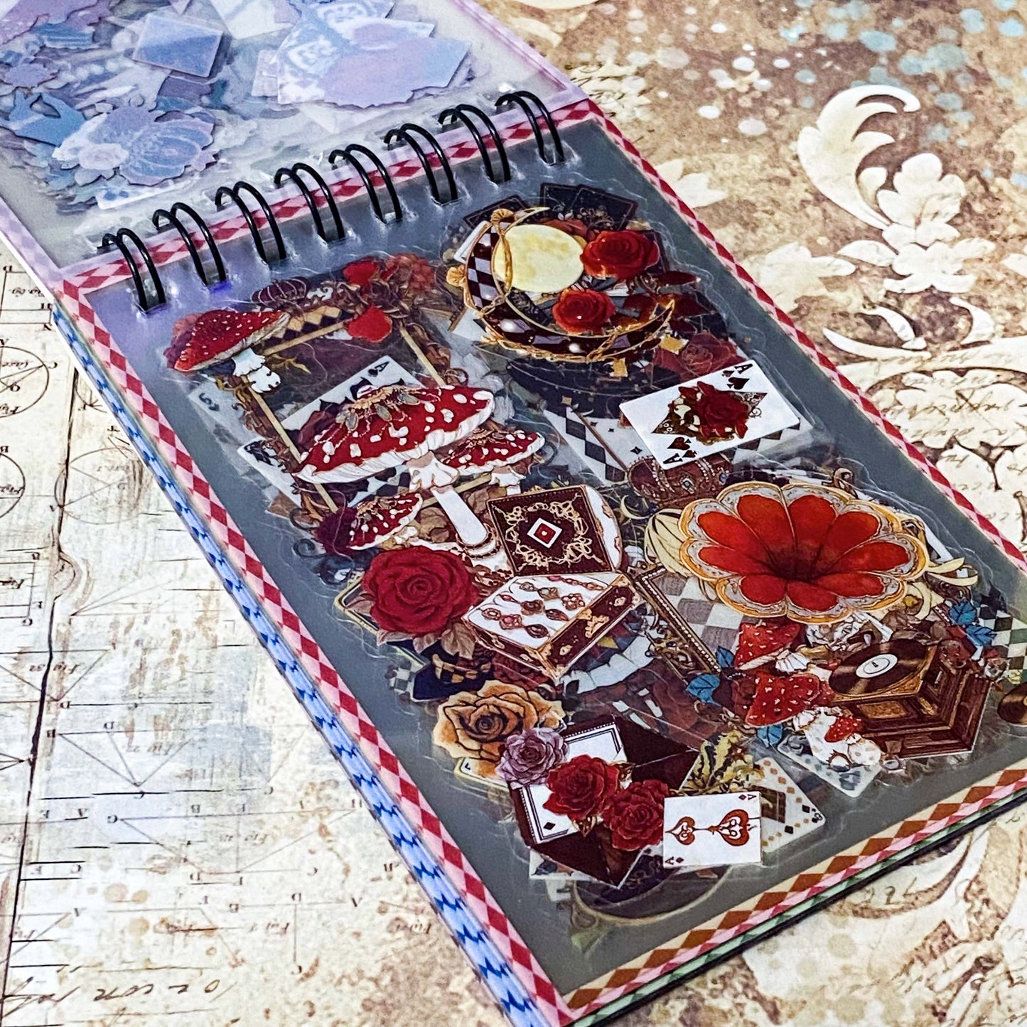 small spiral bound curiouser and curiouser alice clear PET sticker folio featuring fantasy stickers with mushrooms, roses, playing cards, rabbits and vintage gothic fairytale artwork