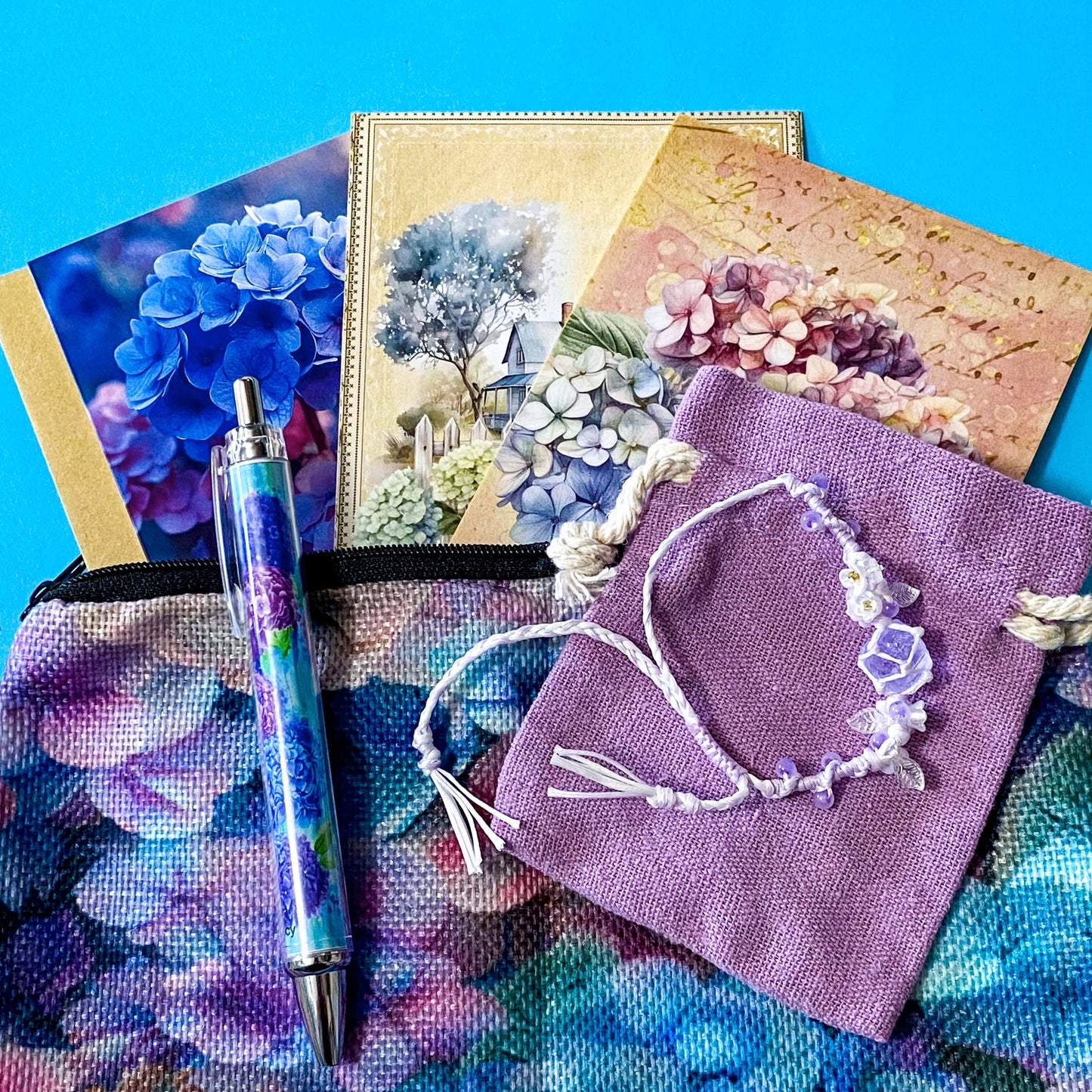 hydrangea whispers midi letterbox gift set with a textured hydrangea pouch, floral ballpoint pen, blank greetings card with kraft envelope, two hydrangeas postcards and an adjustable crystal floral bracelet in a lilac drawstring bag. uk gifts shop.