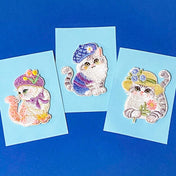 three iron on embroidered cat patches in cute hats on a blue background