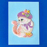 Embroidered fabric patch of a cat wearing a hat on a blue background