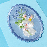 embroidered white rabbit and flowers oval applique patch on a blue background