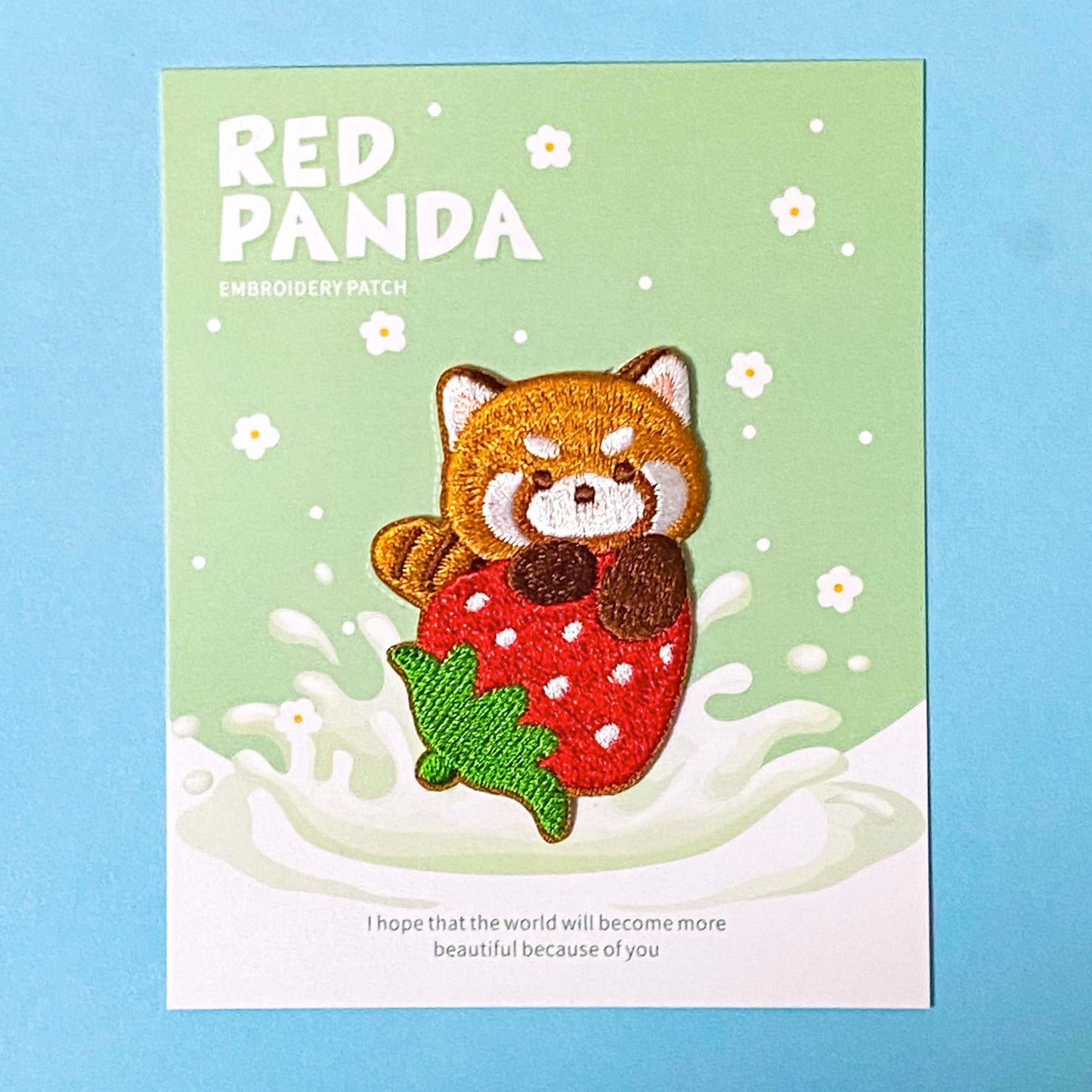 Embroidered patch of a red panda on a strawberry with text on a green card, against a blue background.