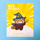 Embroidered patch of a red panda wearing a witch hat on a yellow and blue background.