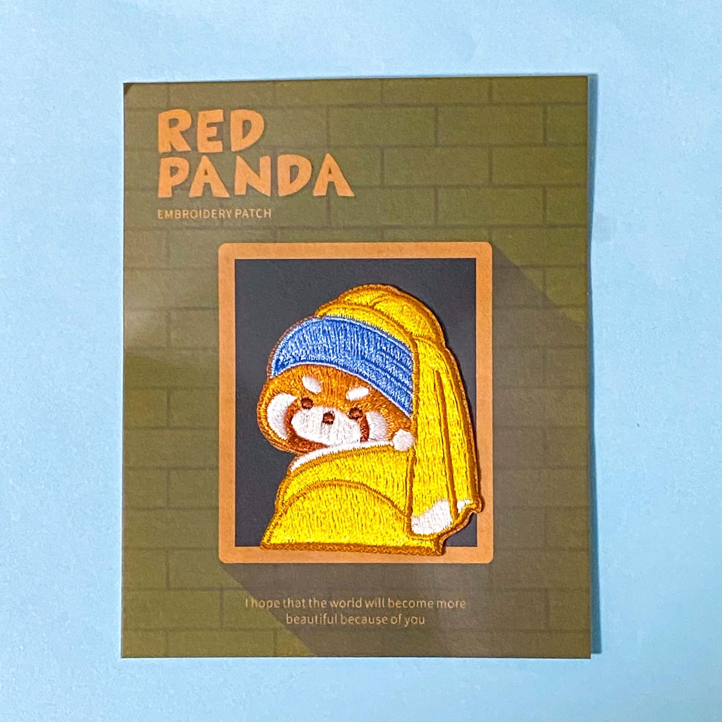 Embroidered patch of a red panda wearing a blue headband and yellow scarf on a green card with 'Red Panda' text. The Girl With The pearl Earring oil painting