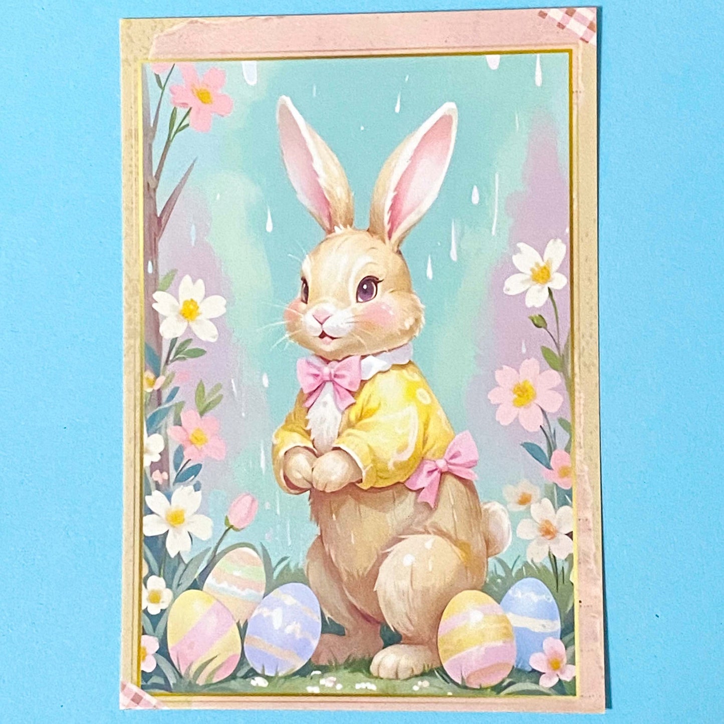 pastel postcard of a bunny with Easter eggs and flowers on a blue background