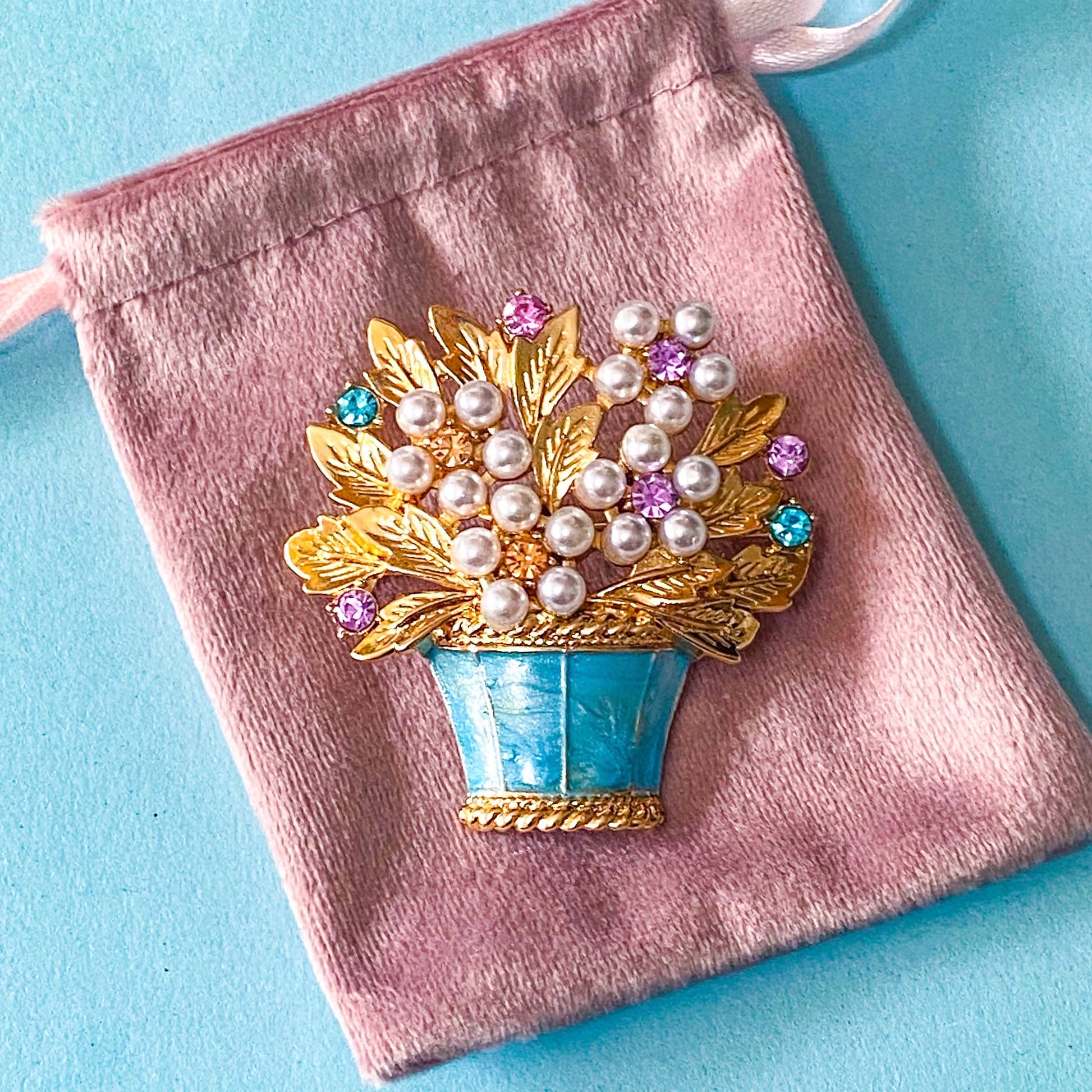 vintage style flower basket brooch with faux pearls and sparkly rhinestones on a velvet pink bag and a blue background