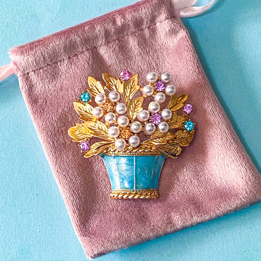 vintage style flower basket brooch with faux pearls and sparkly rhinestones on a velvet pink bag and a blue background