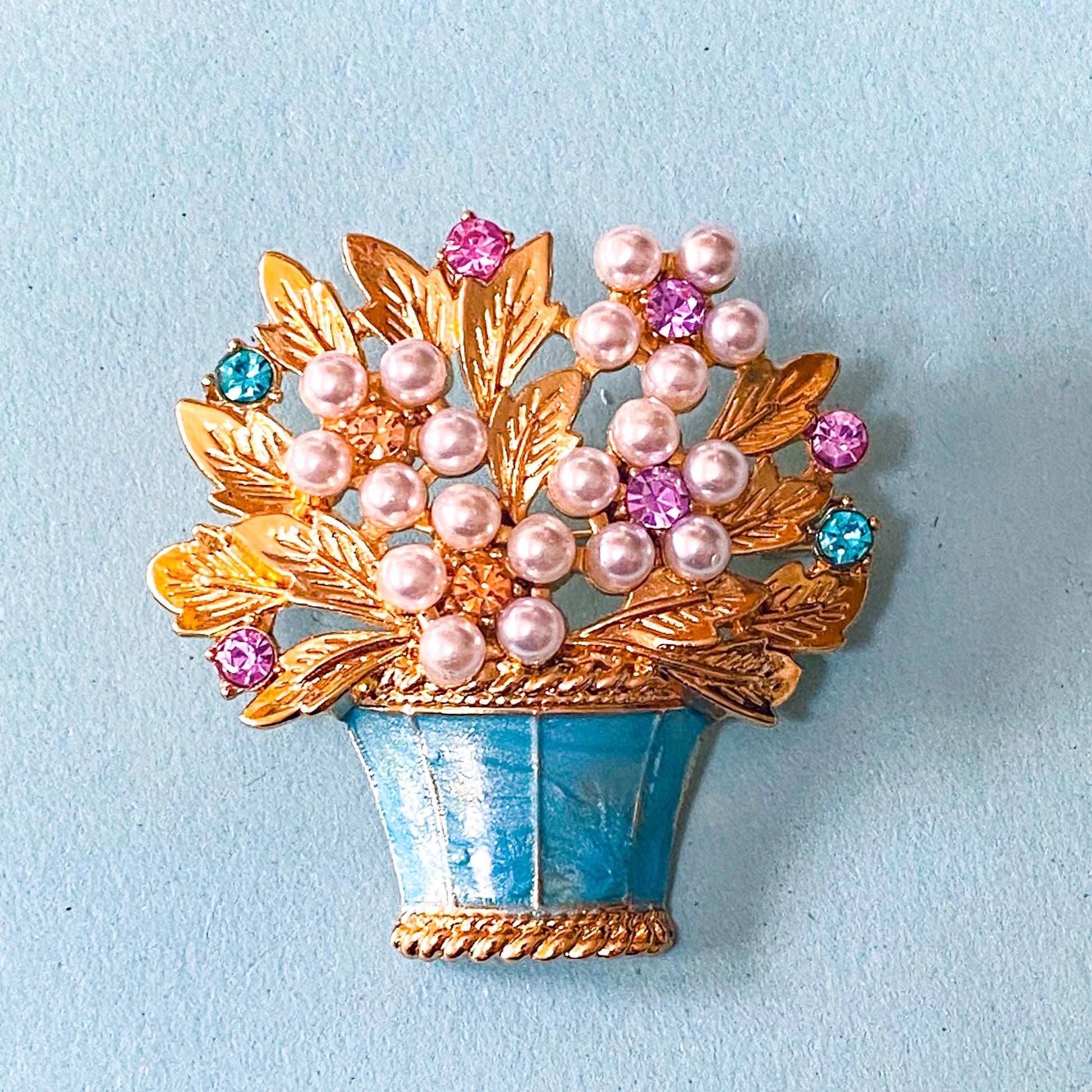 vintage style large gold metal Brooch with pearls and gemstones on a light blue background