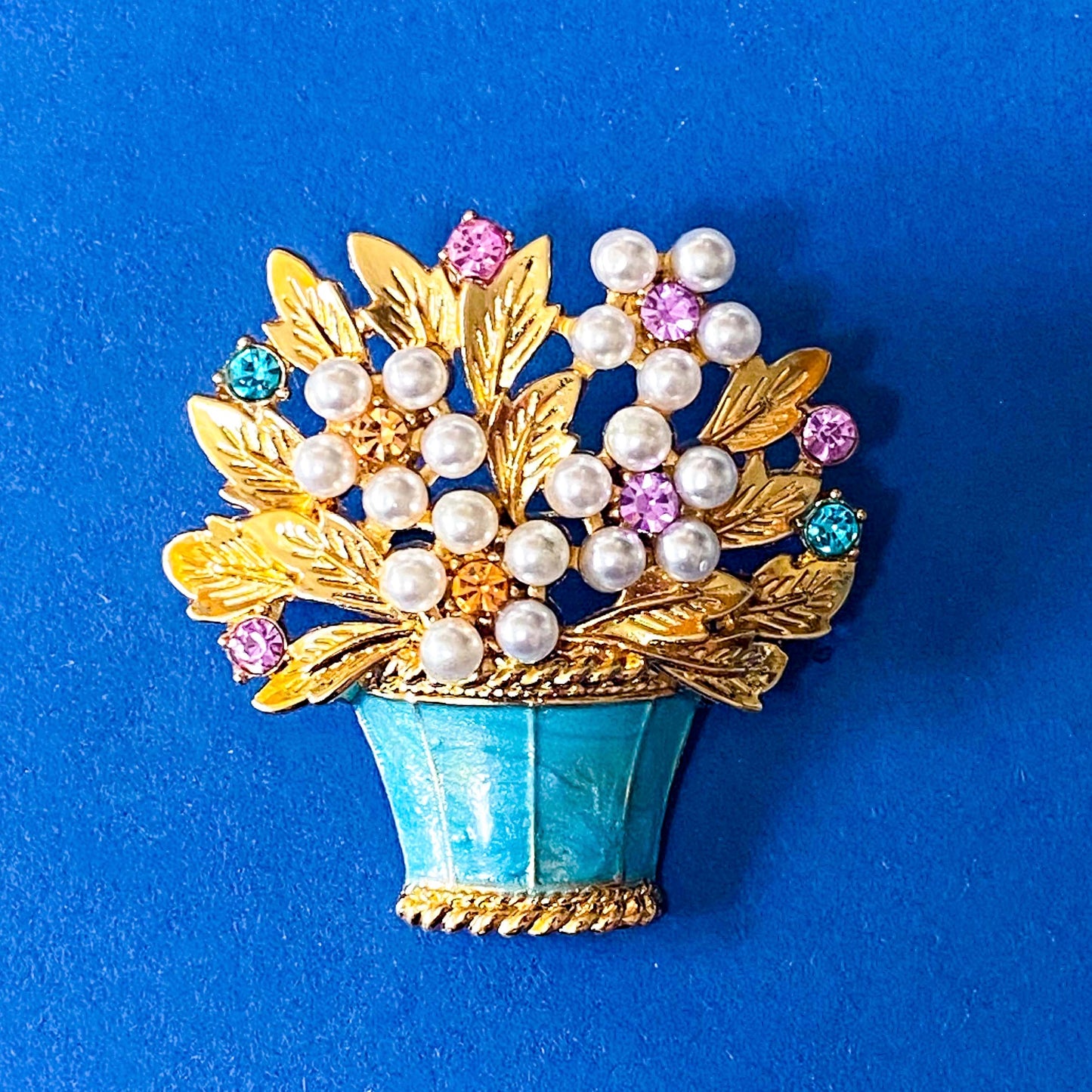 vintage style large turquoise floral brooch with pearls, gemstones, and gold leaves on a blue background