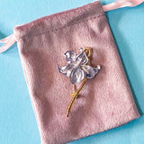 pale silver lilac iris metal brooch on a pink velvet drawstring bag on a blue background