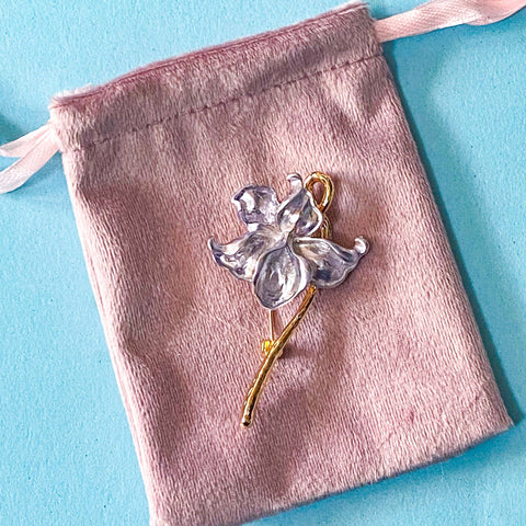 pale silver lilac iris metal brooch on a pink velvet drawstring bag on a blue background