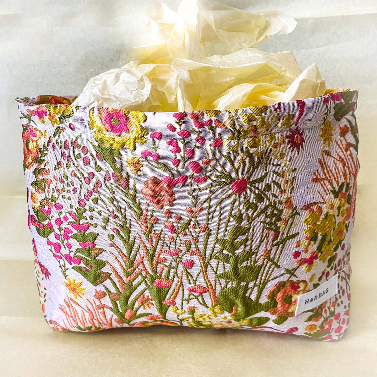 wildflower meadow tapestry pouch with colourful woven floral design including daisies, cream lining, concealed zip closure and gusseted base. Cream, orange, lemon, soft green and white design. Subtle sheen. Large cosmetic bag or toiletry pouch. Uk botanical gift shop.