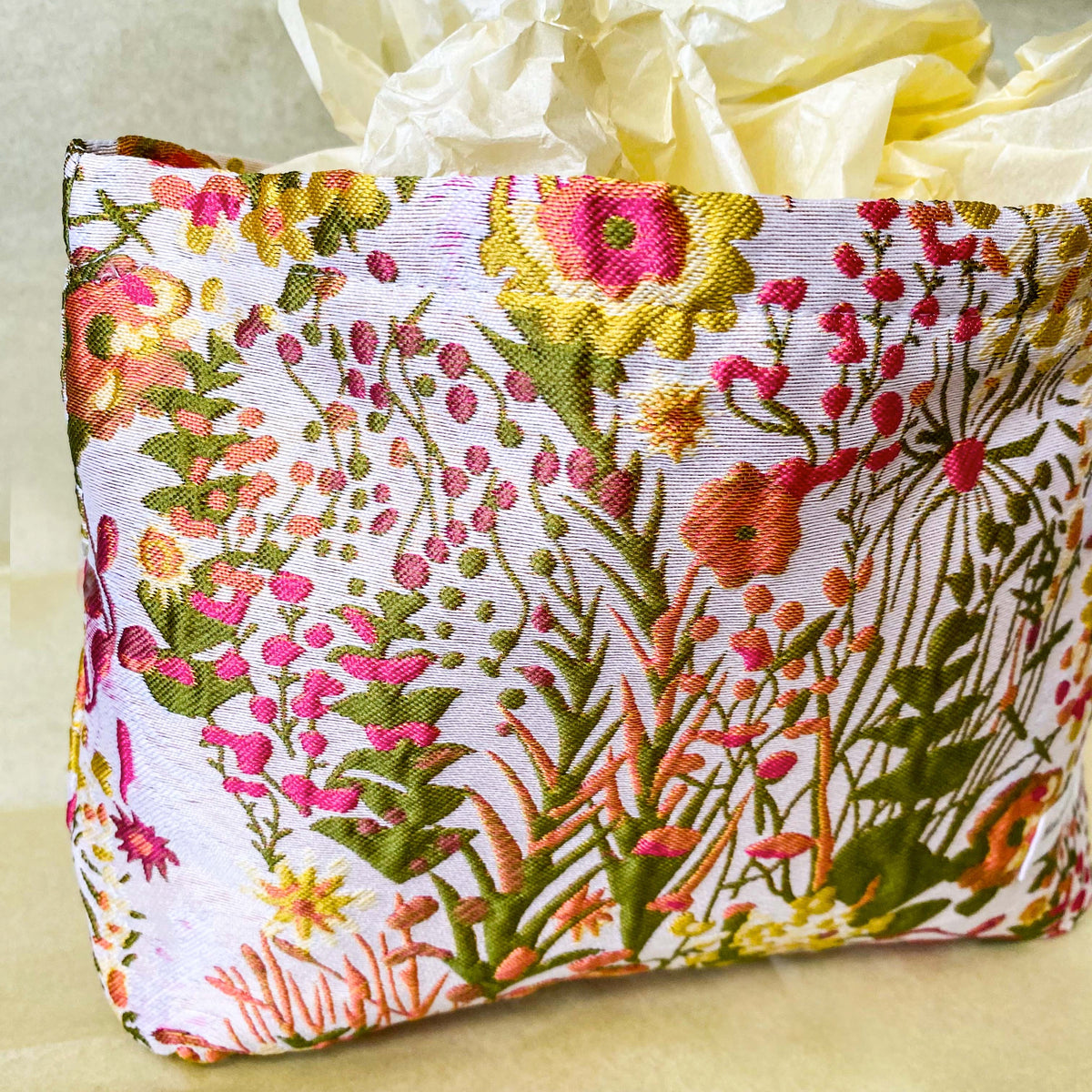 wildflower meadow tapestry pouch with colourful woven floral design including daisies, cream lining, concealed zip closure and gusseted base. Cream, orange, lemon, soft green and white design. Subtle sheen. Large cosmetic bag or toiletry pouch. Uk botanical gift shop.