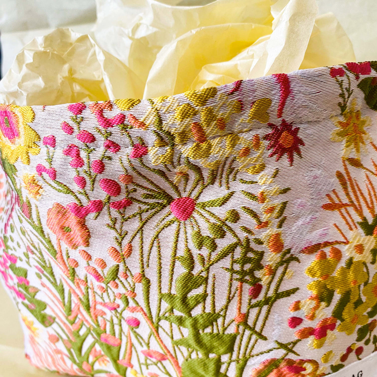 wildflower meadow tapestry pouch with colourful woven floral design including daisies, cream lining, concealed zip closure and gusseted base. Cream, orange, lemon, soft green and white design. Subtle sheen. Large cosmetic bag or toiletry pouch. Uk botanical gift shop.