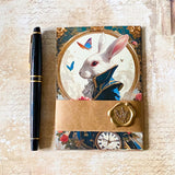alice in wonderland postcard set wrapped in kraft belly band with a wax seal sticker featuring the white rabbit and pocket watch illustration