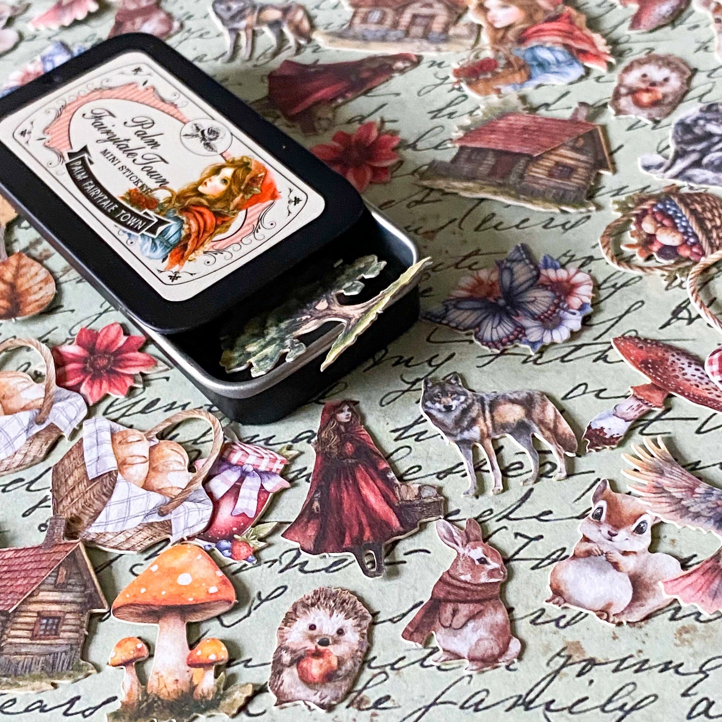 small metal tin of stickers with a vintage red riding hood theme including designs of hedgehog, squirrel, cottage, wolf, mushroom and flowers