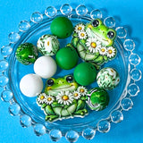 green frog bead bundle with double sided jumbo daisy frog ceramic focal bead and coordinating floral, white and deep green silicone beads on bright blue background