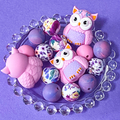 pastel owl silicone bead bundle with marbled purple beads and floral pink beads arranged on a glass plate on a purple background