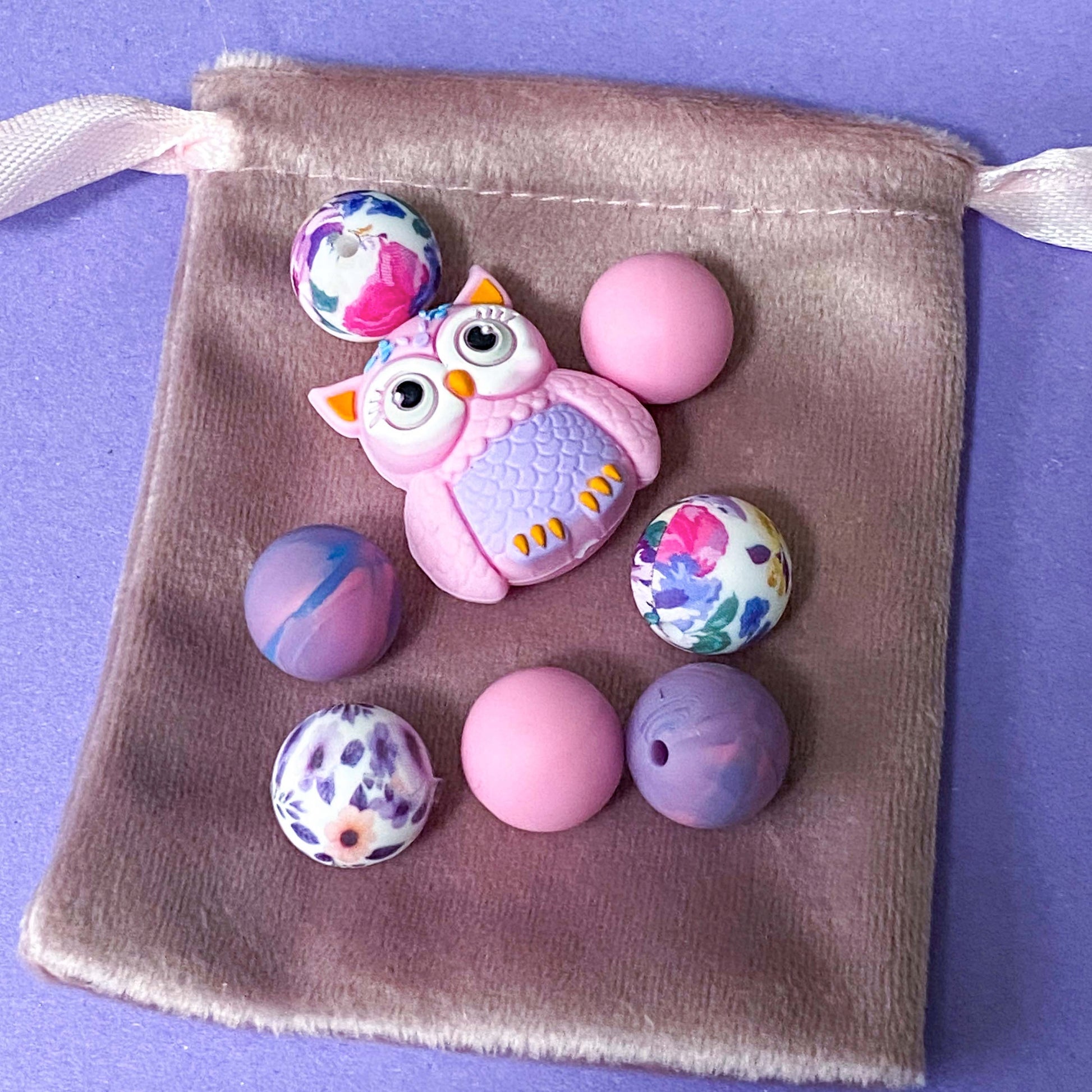 pastel owl silicone bead bundle with marbled purple beads and floral pink beads arranged on a glass plate on a purple background