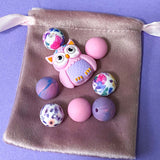 pastel owl silicone bead bundle with marbled purple beads and floral pink beads arranged on a glass plate on a purple background